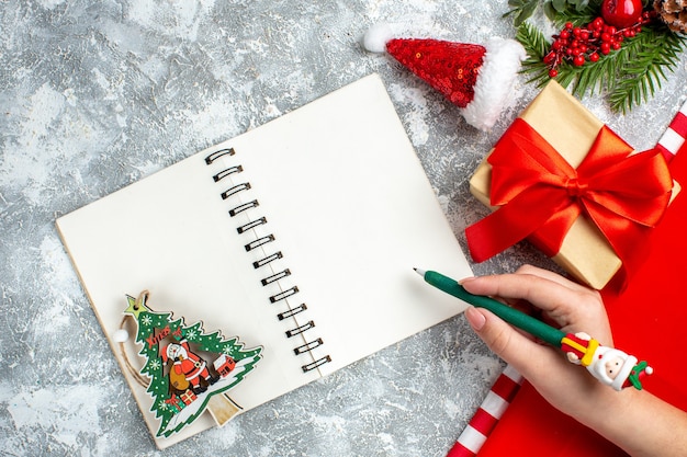 Bovenaanzicht notebook kleine kerstmuts aanwezig groene pen in vrouw hand op grijs witte tafel