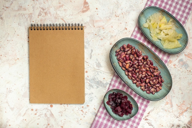 Bovenaanzicht notebook zuurkool bonen gesneden biet op ovale platen op wit en paars geruit tafelkleed op lichtgrijze tafel