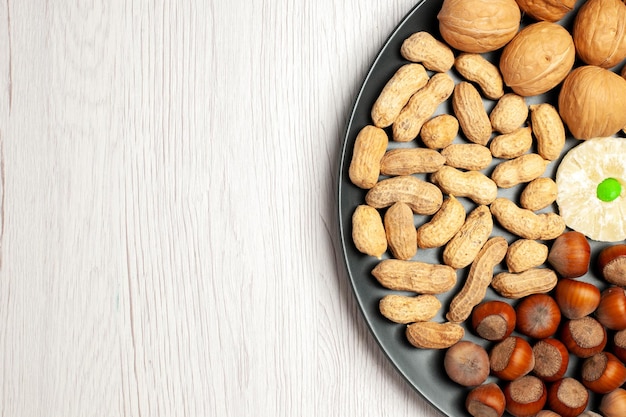 Bovenaanzicht noten samenstelling verse walnoten pinda's en hazelnoten binnen plaat op wit bureau noten snack plant boom veel shell