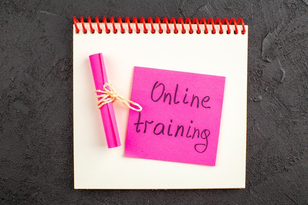 Bovenaanzicht online training geschreven op roze plaknotitie op notitieblok op zwart