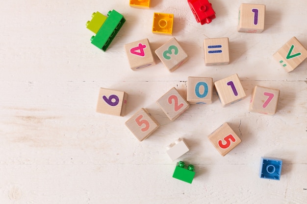Bovenaanzicht op houten kubussen met cijfers en kleurrijke plastic bakstenen op witte houten tafel achtergrond