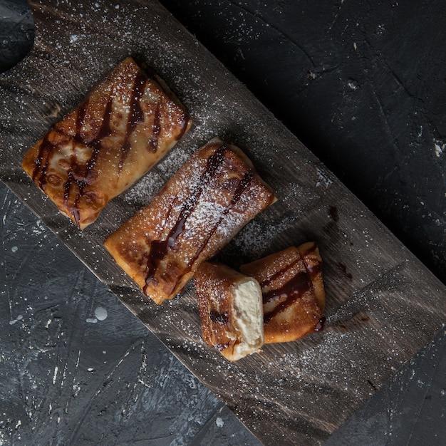 Bovenaanzicht pannenkoeken met chocoladesiroop en poedersuiker in snijplank