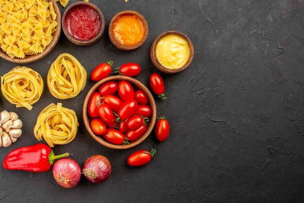 Bovenaanzicht pasta en tomaten kommen pasta en tomaten ui knoflook drie soorten sauzen op tafel