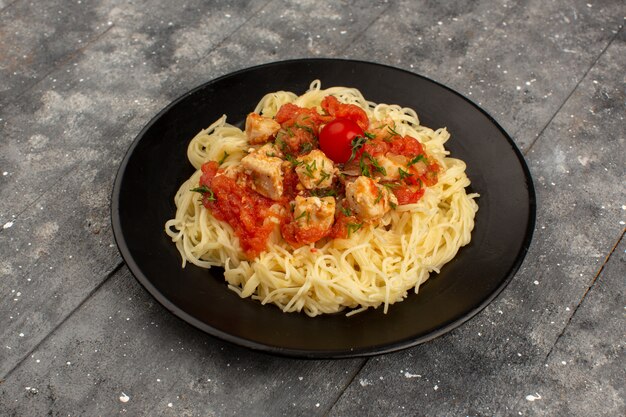 bovenaanzicht pasta geel gekookt met kippenvleugels en tomatensaus in zwarte plaat op de grijze houten rustiek