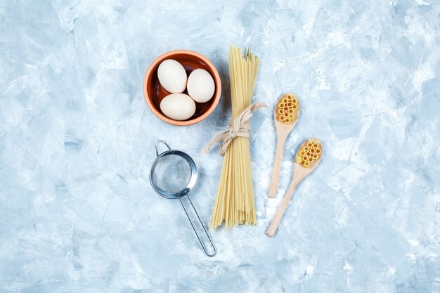 Bovenaanzicht pasta in houten lepels met eieren, zeef op grungy grijze achtergrond. horizontaal