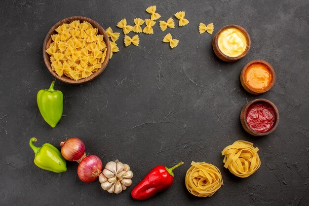 Bovenaanzicht pasta pasta in kom kleurrijke sauzen groene en rode bal peper knoflook ui zijn neergelegd in een cirkel op de zwarte tafel