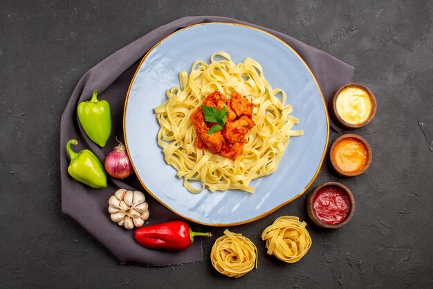 Bovenaanzicht pastakommen met sauzen pasta kleurrijke bal peper knoflook ui naast de smakelijke pasta met vlees en kruiden op het tafelkleed