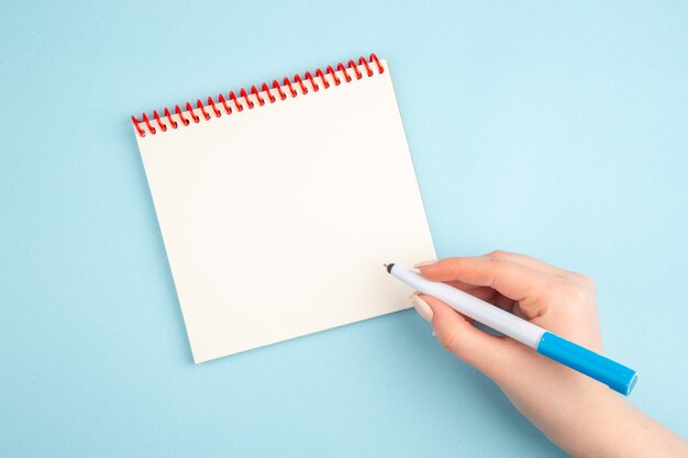 Bovenaanzicht pen in de hand notitieblok op blauw