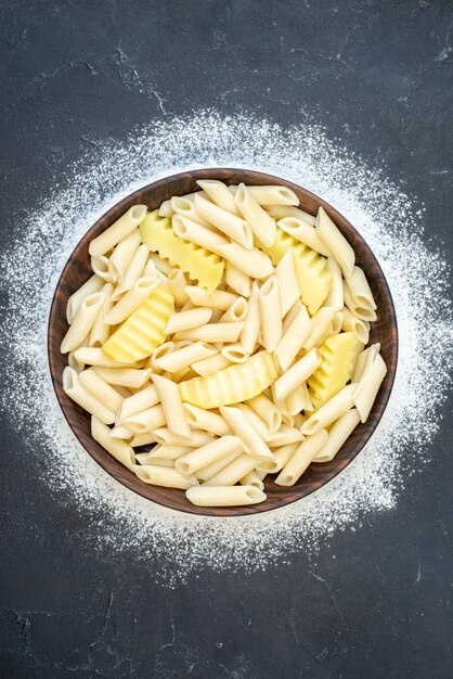 Bovenaanzicht penne pasta met aardappel in kom bestrooide bloem op donkere tafel