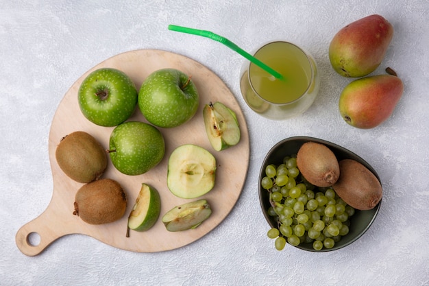 Bovenaanzicht peren met kiwi en druiven in een kom met groene appelschijfjes op een stand met appelsap op een witte achtergrond