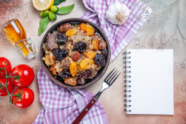 Bovenaanzicht pilaf witte notebook tomaten knoflook citroen olie vork pilaf op het tafellaken