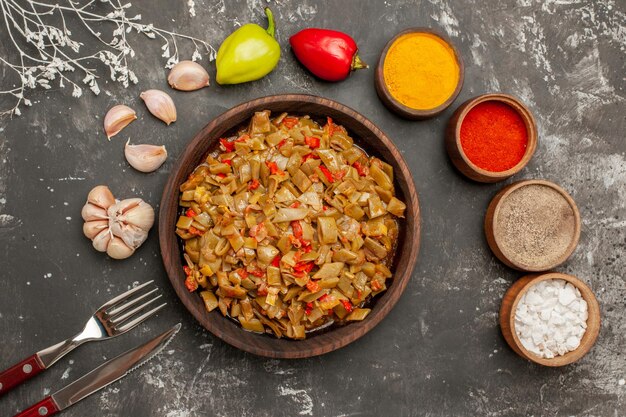 Bovenaanzicht plaat op de tafel kommen van kleurrijke kruiden tomaten knoflook bal peper smakelijk gerecht van sperziebonen naast de vork en mes op de donkere tafel