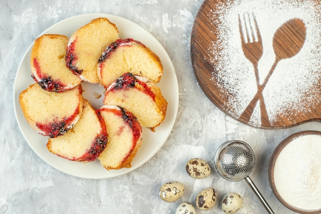 Bovenaanzicht plakjes jam cake op bord kwarteleitjes vork en lepel bedrukt op een houten bord met bloem