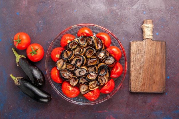 Bovenaanzicht plantaardige maaltijd gesneden en gerolde tomaten met aubergines op de donkere achtergrond