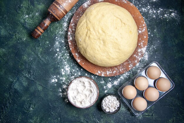 Bovenaanzicht rauw deeg met witte bloem en eieren op een donkerblauwe achtergrond gebak bak cake rauw ovendeeg hotcake pie vers