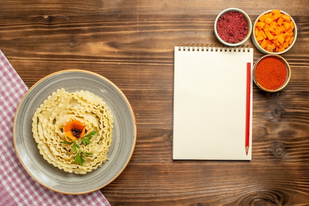 Gratis foto bovenaanzicht rauwe deeg pasta met verschillende kruiden op de bruine tafel deeg rauwkost pastamaaltijd