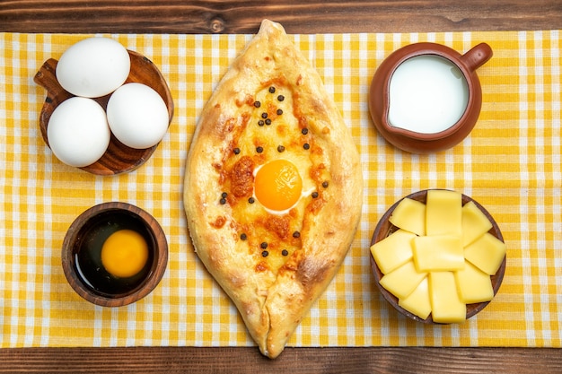 Bovenaanzicht rauwe eieren met gesneden kaas ei brood en melk op houten oppervlak product eieren deeg maaltijd eten rauw