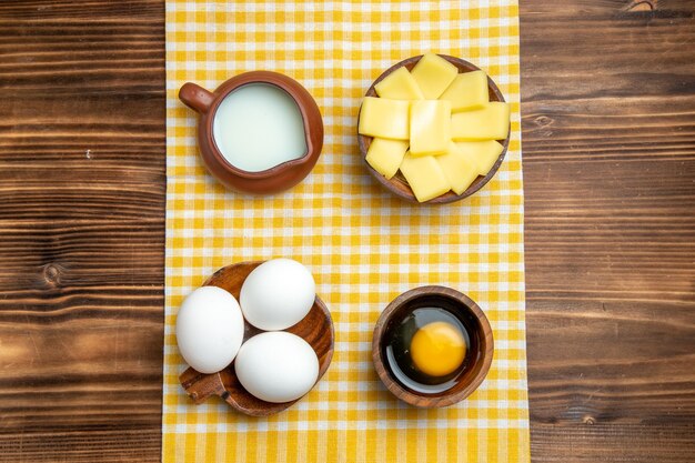 Bovenaanzicht rauwe eieren met gesneden kaas en melk op houten oppervlak product eieren deeg maaltijd rauw voedsel