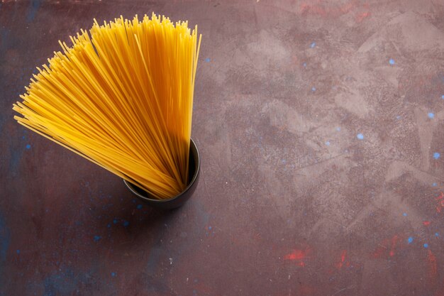 Bovenaanzicht rauwe italiaanse pasta lang gevormd geel gekleurd op de donkere achtergrond pasta italië deeg maaltijd rauwkost kleur