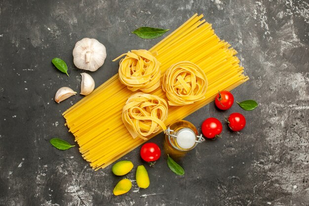 Bovenaanzicht rauwe Italiaanse pasta met knoflook en tomaten op lichtgrijze achtergrond