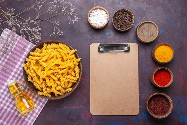 Bovenaanzicht rauwe Italiaanse pasta met verschillende kruiden op de donkere kleur van het ingrediënt van de maaltijd van het voedsel van de oppervlaktedegas