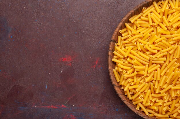 Bovenaanzicht rauwe italiaanse pasta weinig gevormd op donkere bureau groenten pasta maaltijd kleur van het voedsel