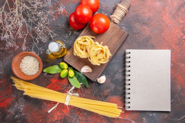 Bovenaanzicht rauwe pasta met olie en tomaten op donkere oppervlak deeg rauwe pasta