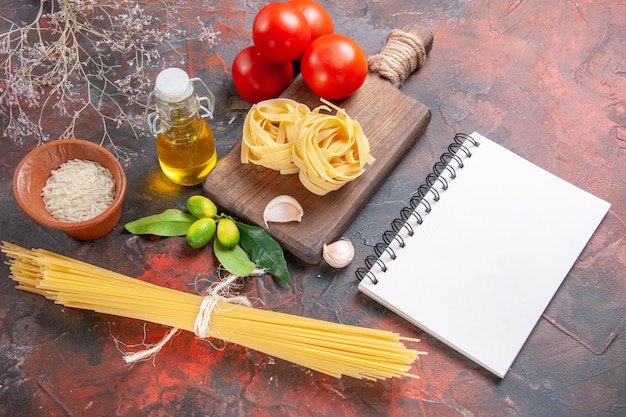 Bovenaanzicht rauwe pasta met olietomaten en knoflook op donker bureau rauw pastadeeg