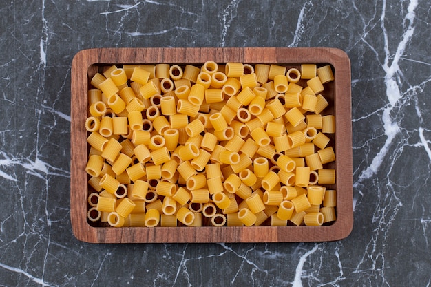 Bovenaanzicht rauwe pasta penne op houten plaat.