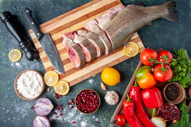 Bovenaanzicht rauwe vis plakjes mes op snijplank groenten op houten serveerplank pepermolen op keukentafel