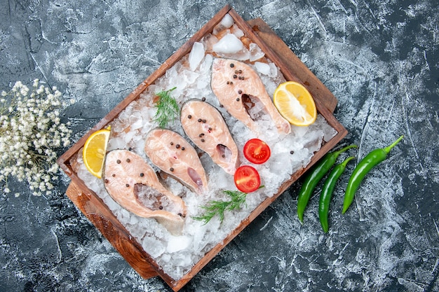 Bovenaanzicht rauwe vis plakjes met ijs op houten bord groene hete pepers op tafel