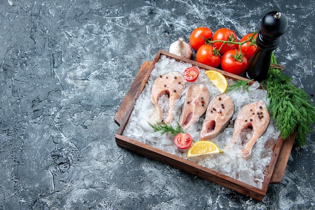 Bovenaanzicht rauwe visplakken met ijs op houten bord tomaten knoflook dille op tafel kopie plaats