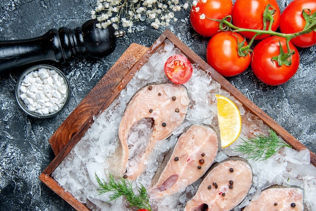 Bovenaanzicht rauwe visplakken met ijs op houten bord tomaten zeezout in kleine kom op tafel