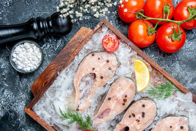 Bovenaanzicht rauwe visplakken met ijs op houten bord tomaten zeezout in kleine kom op tafel