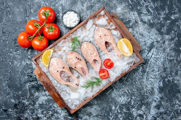 Bovenaanzicht rauwe visplakken met ijs op houten bord tomaten zeezout op tafel met vrije ruimte