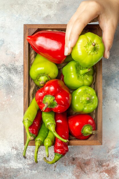 Bovenaanzicht rode en groene paprika's hete pepers in houten doos paprika in vrouw hand op naakt oppervlak