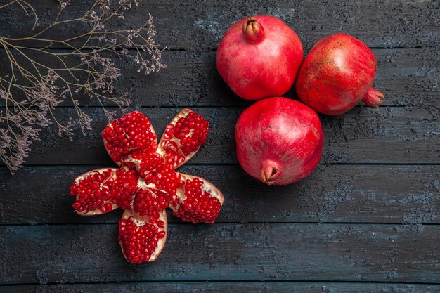 Bovenaanzicht rode granaatappels gepilde granaatappel naast boomtakken en drie granaatappels op donkere ondergrond