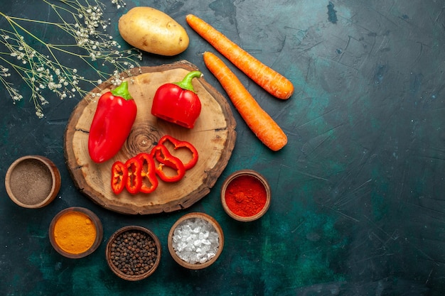 Bovenaanzicht rode paprika met verschillende kruiden op donkergroen oppervlak plantaardig pittig warm eten