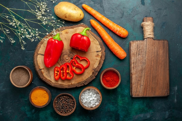 Bovenaanzicht rode paprika met verschillende kruiden op donkergroene groenten pittig warm eten