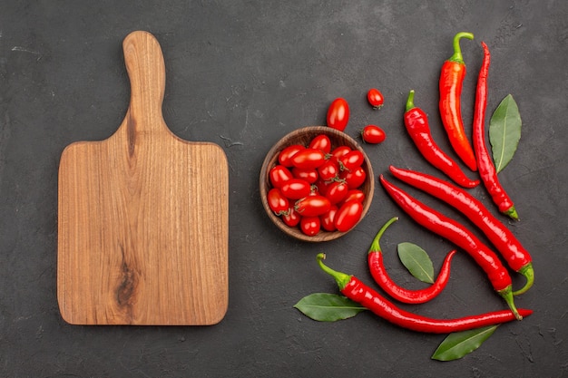 Bovenaanzicht rode paprika's en loonblaadjes en een kom met kerstomaatjes en een snijplank op zwarte tafel met kopie ruimte