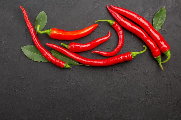 Bovenaanzicht rode paprika's en loonblaadjes op zwarte grond met vrije ruimte