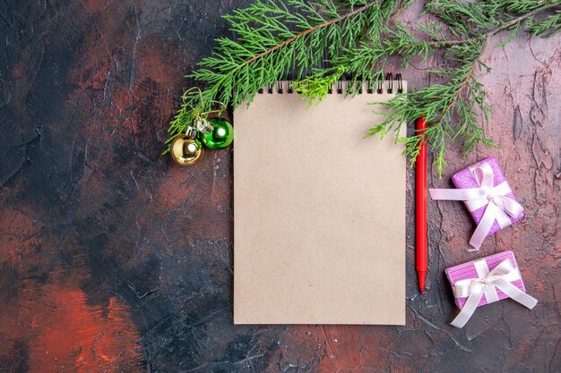 Bovenaanzicht rode pen een blocnote pijnboomtakken kerstboom speelgoed en geschenken op donkerrode oppervlakte vrije ruimte