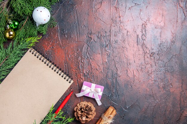 Bovenaanzicht rode pen een notebook dennenboom takken kerstboom bal speelgoed op donkerrood oppervlak vrije ruimte