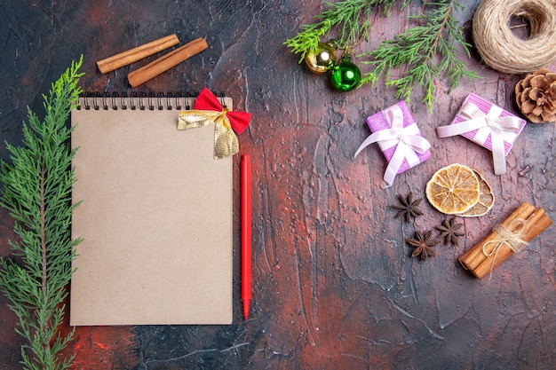 Bovenaanzicht rode pen een notebook pijnboomtakken kerstboom ballen stro draad kaneel steranijs Kerstcadeaus op donkerrood oppervlak