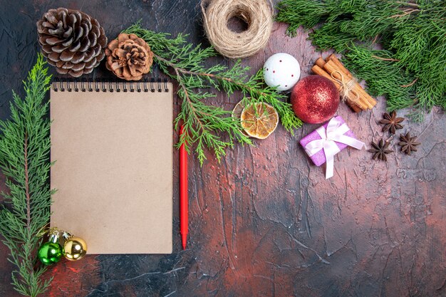 Bovenaanzicht rode pen een notitieboekje pijnboomtakken kerstboom bal speelgoed en cadeau kaneel anijs stro draad op donkerrood oppervlak vrije plaats