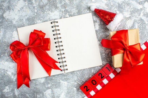 Bovenaanzicht rode strik op notebook houtblokken kleine kerstmuts op grijs witte tafel