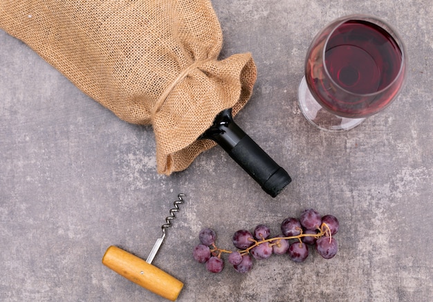 Bovenaanzicht rode wijn in jute zak met glas en druif op donkere horizontale steen