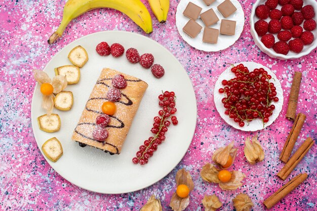 Bovenaanzicht rol cake plakjes met verschillende vruchten in witte plaat op de gekleurde achtergrond koekjes zoete kleur