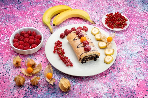 Bovenaanzicht roll cake met fruit bananen in witte plaat op de gekleurde achtergrond cake biscuit zoete kleur