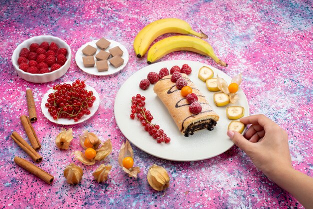 Bovenaanzicht roltaart met fruit in witte plaat op de gekleurde zoete kleur van het koekjekoekje van het bureau